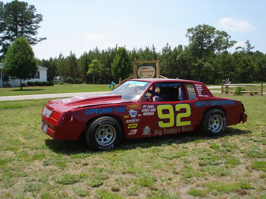 Red number 92 stock car parked in a grassy yard