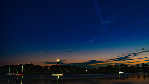 A comet and stars above sailboats at twilight